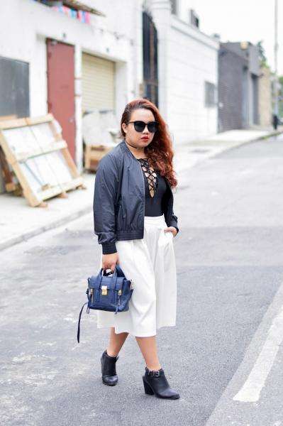 A young woman poses outside wearing a black top, sunglasses.