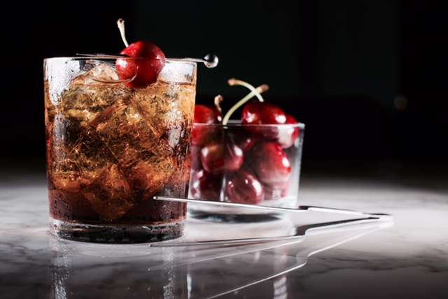 A cocktail with a cherry garnish, displayed against a black background. 