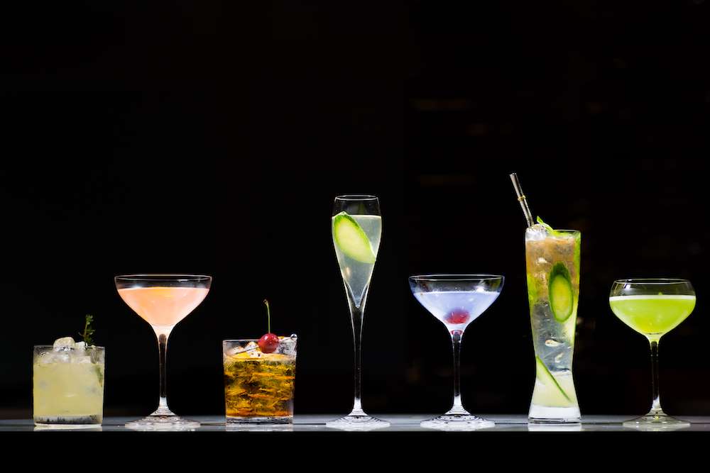 Five different cocktails displayed on a counter against black background.