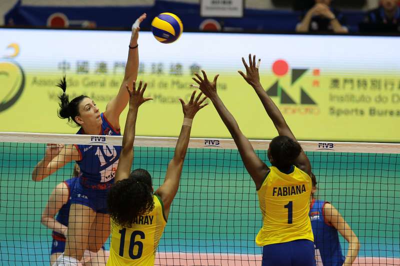 Players leap for the ball at the net during volleyball game. 