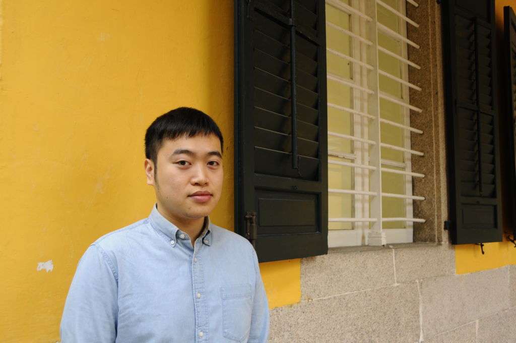 Photographer Tang Kuok Hou in Macau posing against yellow backdrop on the street.