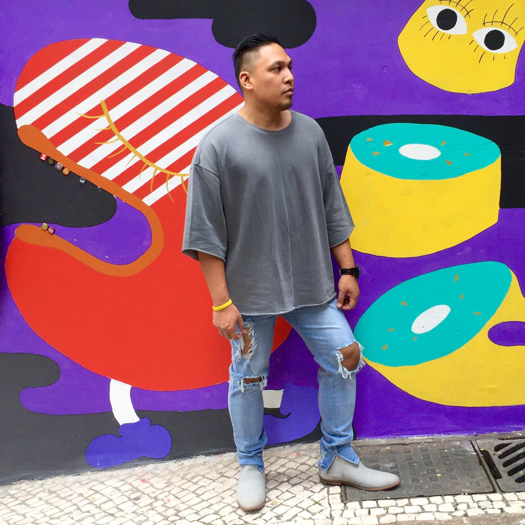 A young man posing outside on street in Macau, wearing a grey t-shirt and ripped light colored bluejeans. '