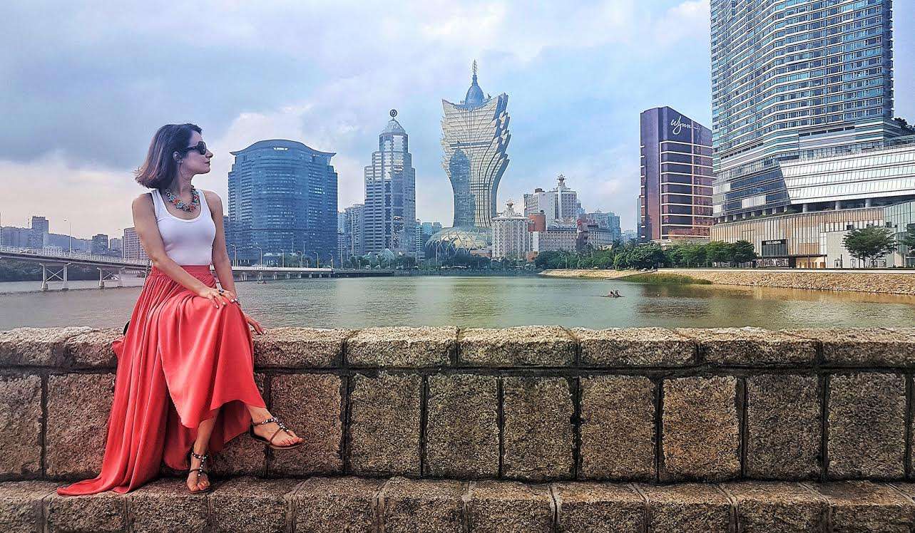 Andreia Neto posing in long red skirt against backdrop of Macau cityscape. 