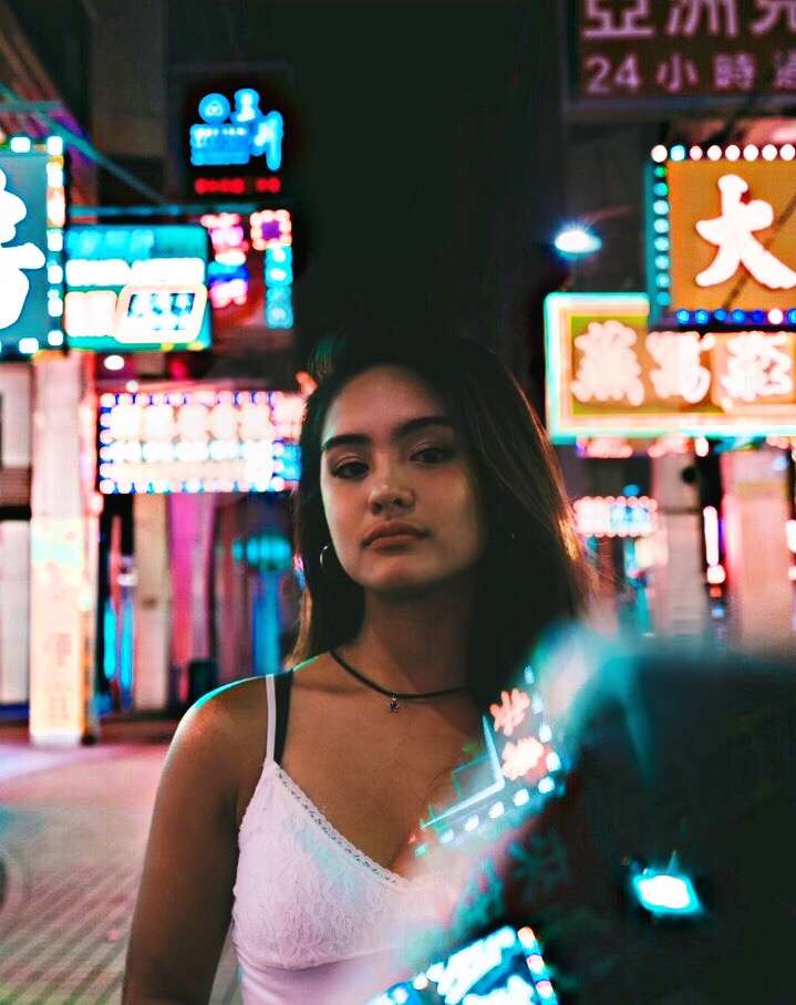 A closeup shot of Enya Escote on the street in Macau at night, wearing a white lace top.