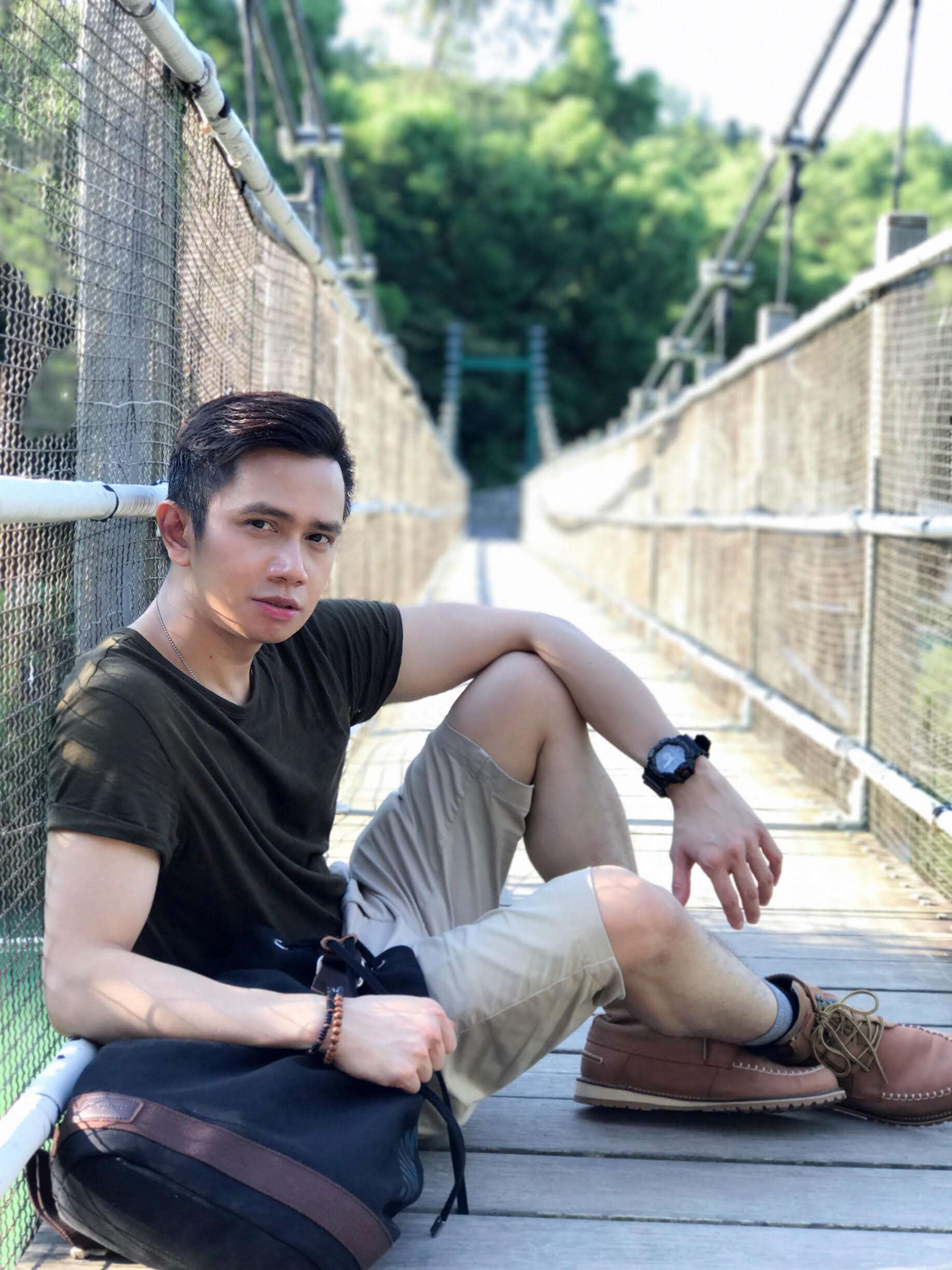 Louis Quizon poses outside in Macau wearing an olive t-shirt, tan shorts, and light brown shoes.
