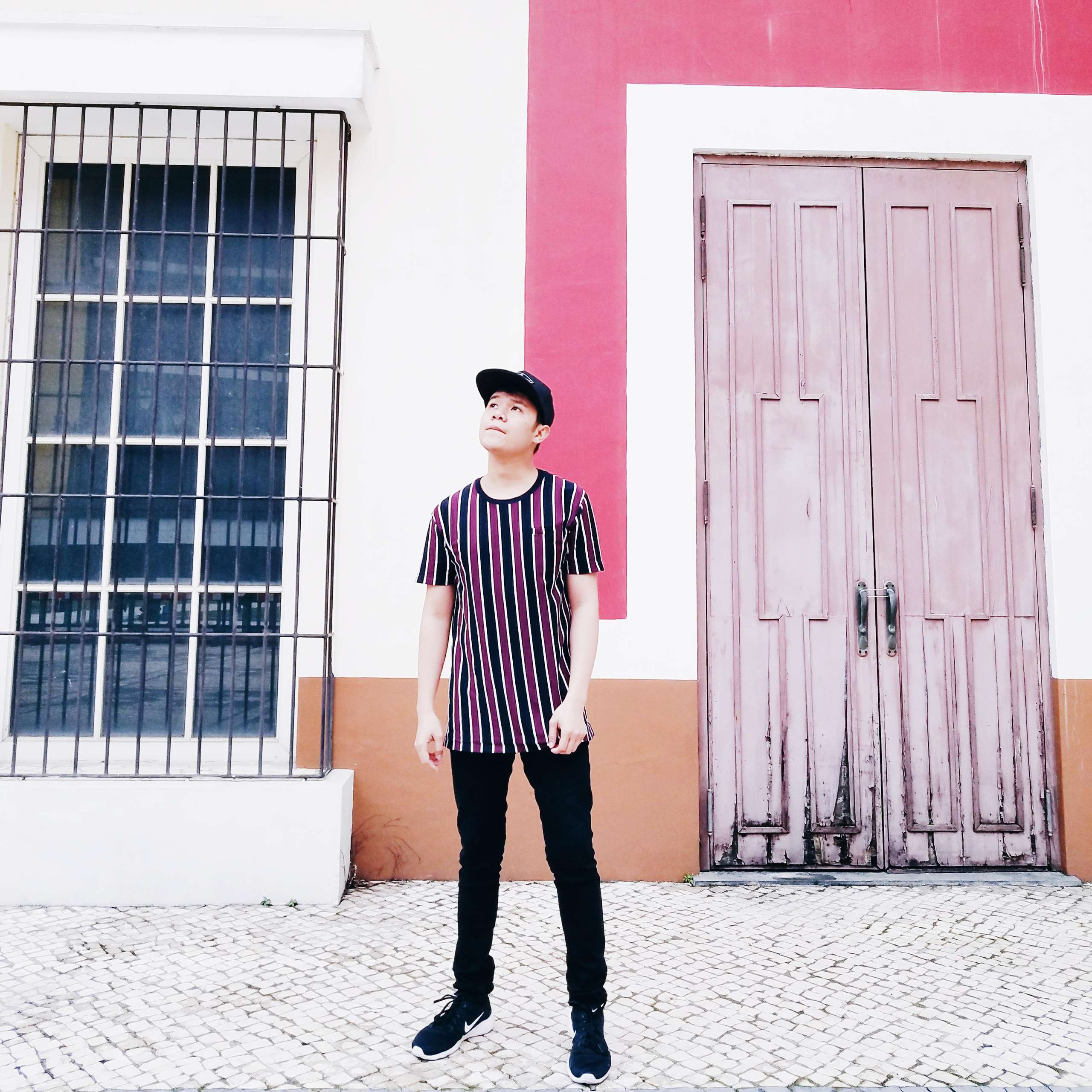 A young man poses on a street in Macau wearing a horizontally striped shirt and dark trousers.