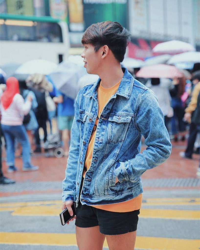 Patrick Dungo outside in Macau wearing a denim jacket, yellow t-shirt, and black shorts.