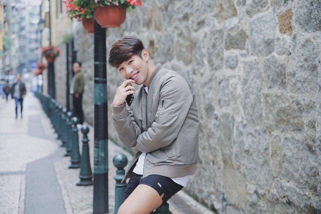 Patrick Dungo poses outside on the street in Macau, wearing a grey top and black shorts.
