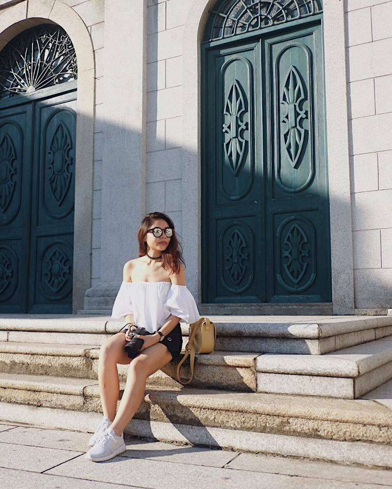 Girl posing on steps wearing dark shorts, white top, and sun glasses in Macau.