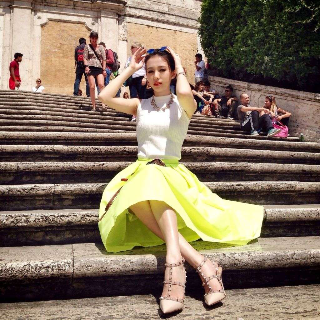 A girl in Macau poses on steps wearing a white top and lime green skirt.