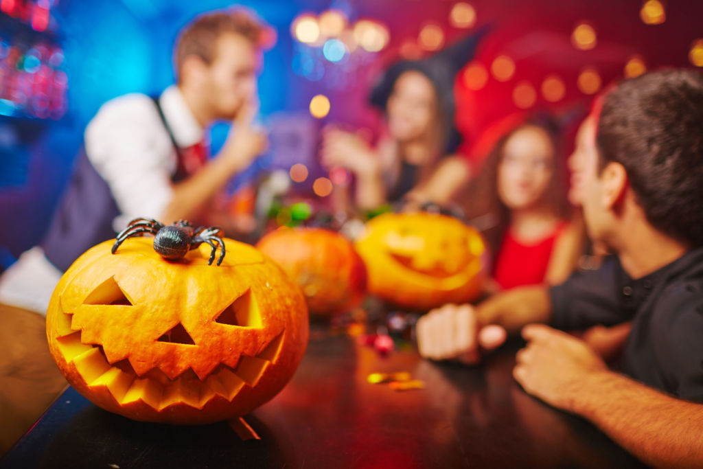 A carved pumpkin sits on a table with party going in background