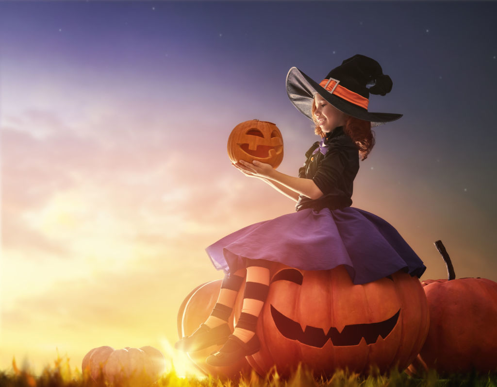 A young girl sits on a large pumpkin while holding a small pumpkin. 