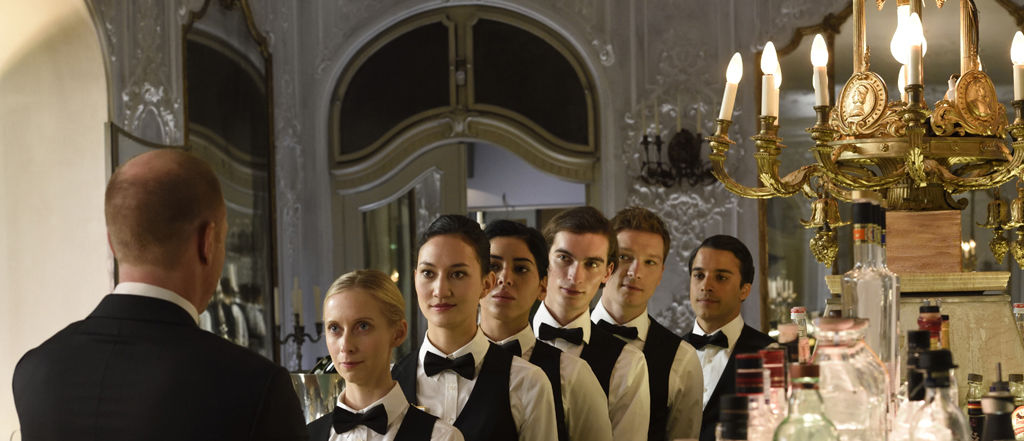 Waitstaff lined up before a restaurant manager in a scene from a German film. 