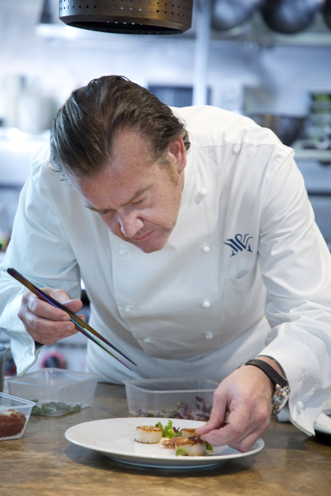 Chef Michael White bent down and carefully plating a dish in his kitchen