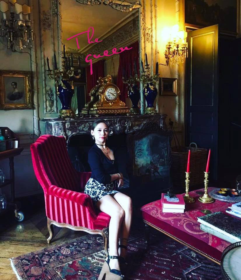 A woman wearing a skirt sits in a red upholstered living room chair. 