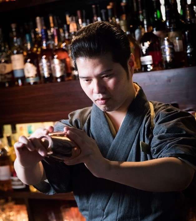 A bartender holding a cocktail shaker while making a drink. 