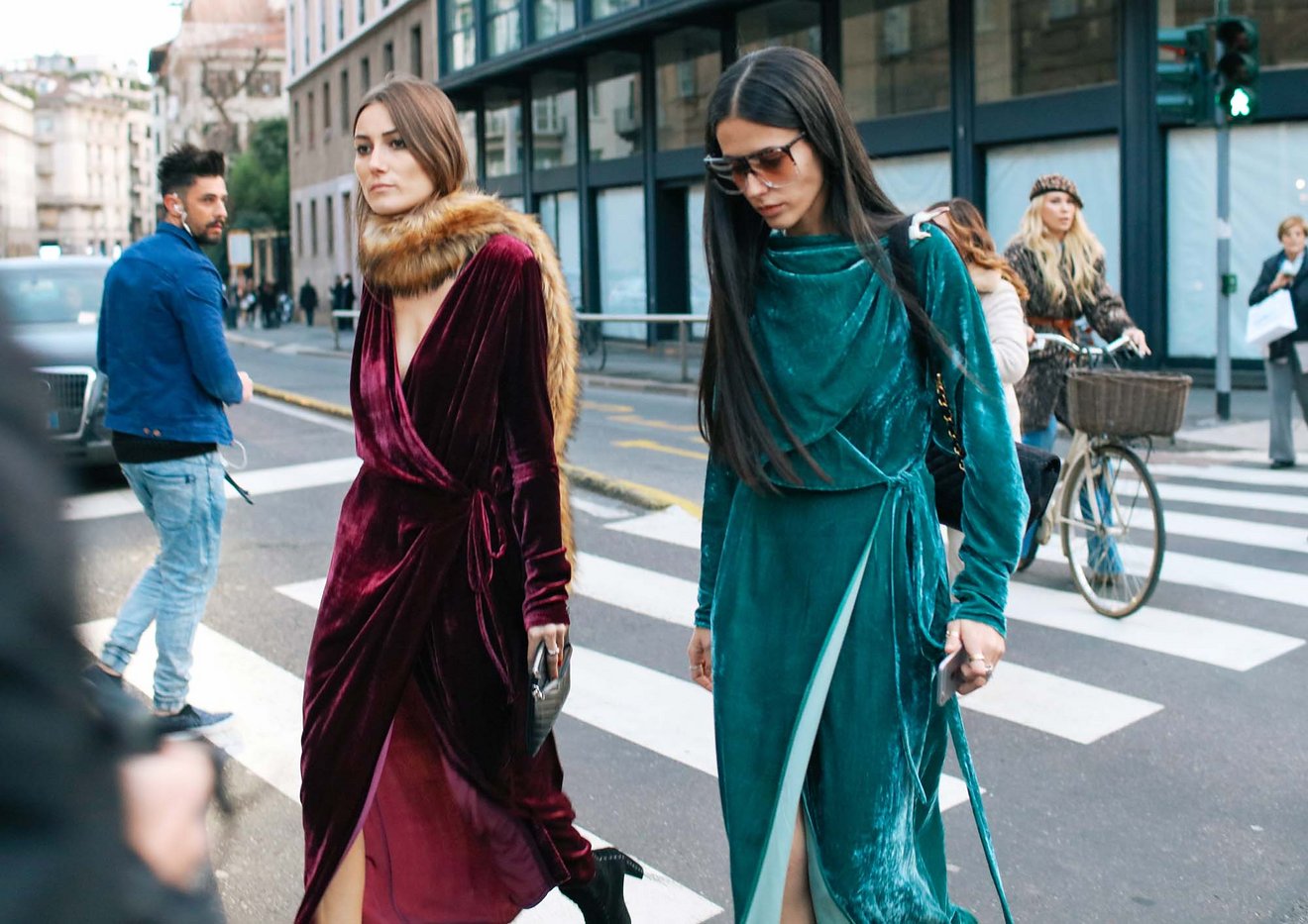 Two women modeling long velvet gowns and walking on the street. 