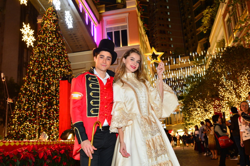 A man and woman pose in costume against a backdrop of Christmas lights on the street in Hong Kong. 