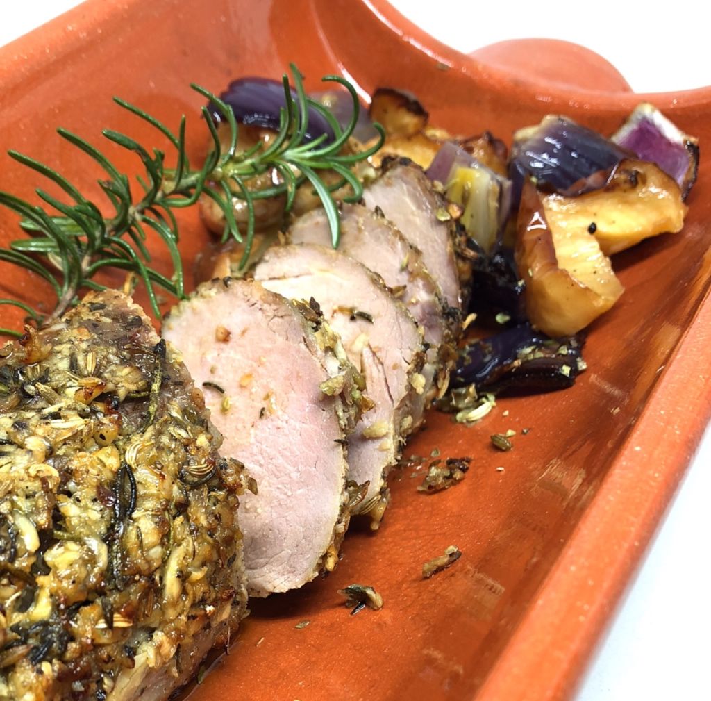 A roasted pork loin sliced on a wooden serving tray. 